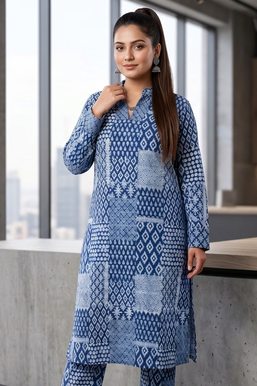 A woman modeling a blue and white patterned kurta and trouser set in a modern indoor setting with large windows and concrete walls.