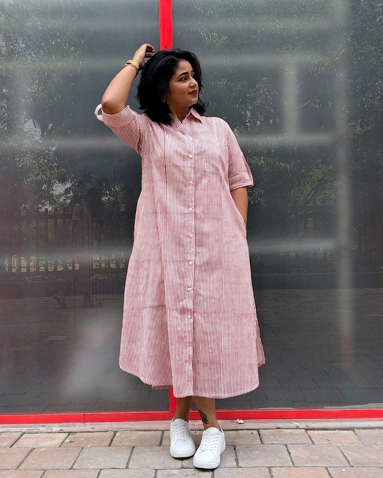 Woman wearing a pink striped dress standing against a reflective glass wall.