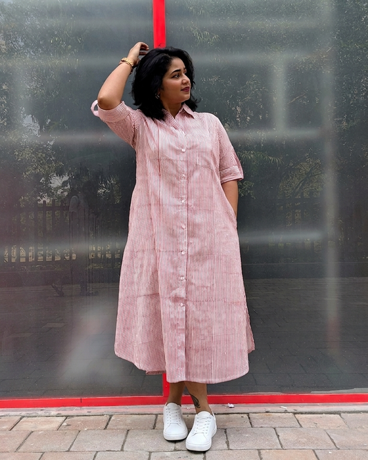 Woman wearing a pink striped dress standing against a reflective glass wall.
